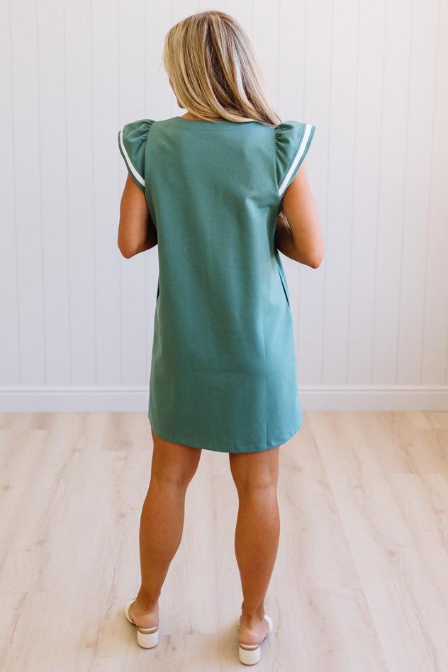 Woman wearing a green dress with white trim in a minimal indoor setting