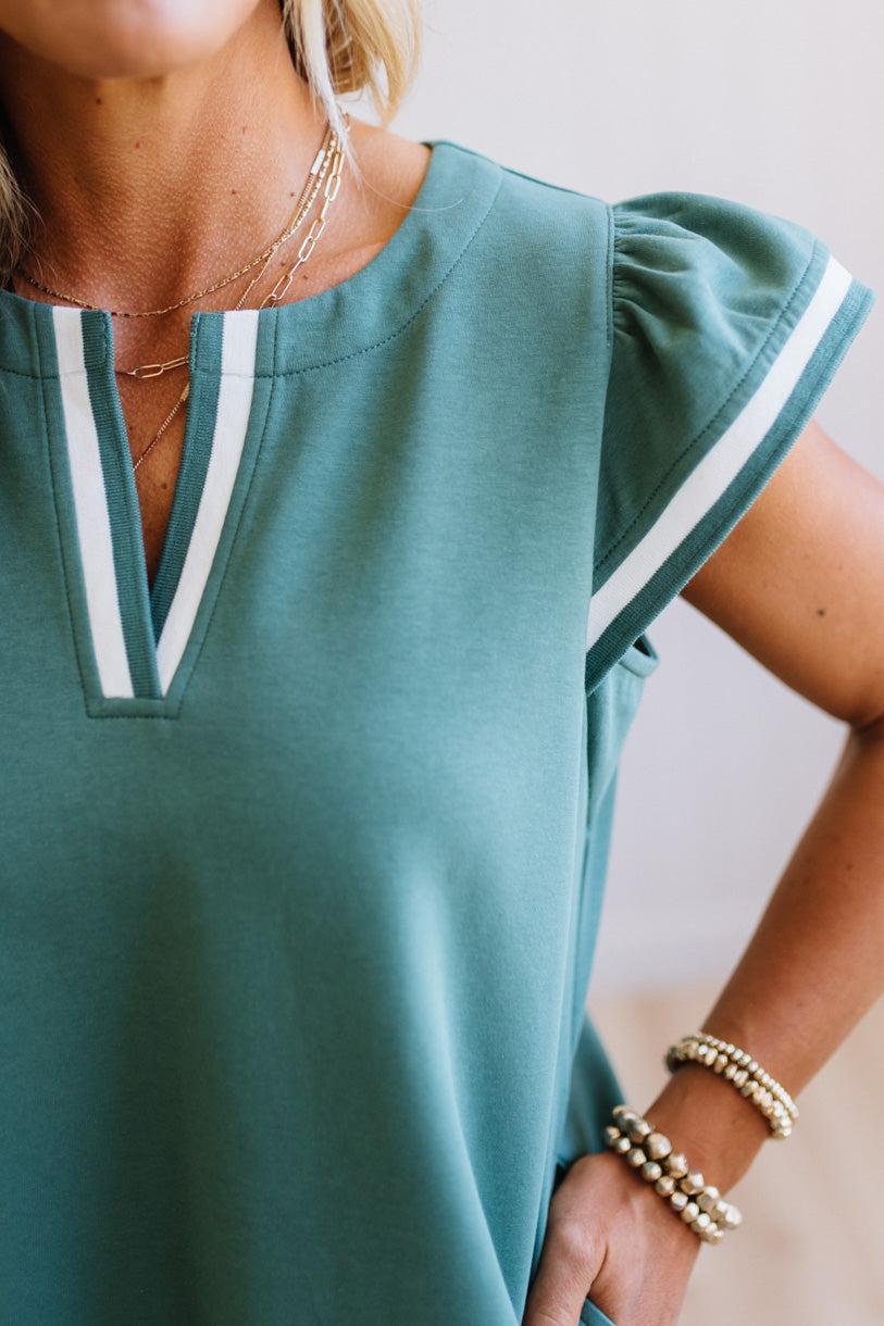 Green top with white trim worn by a person, with a neutral background