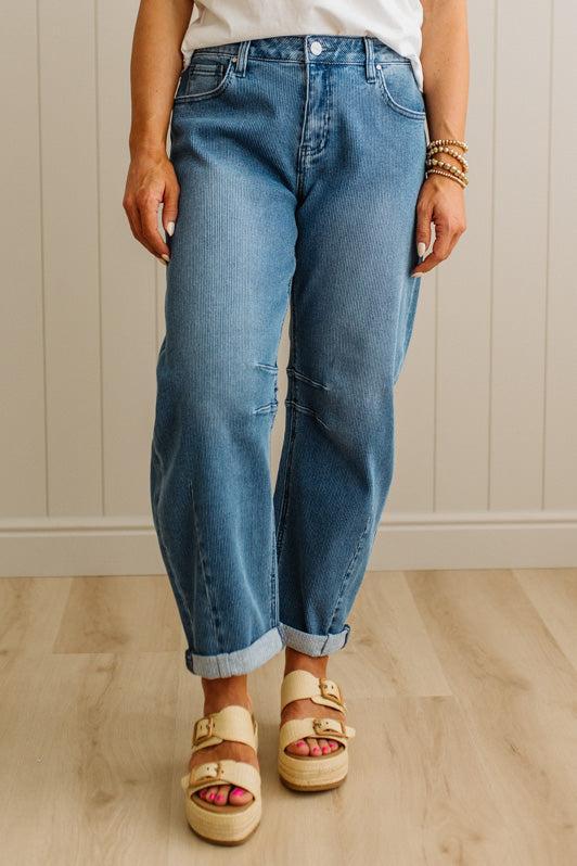 Person wearing blue jeans and sandals standing on a wooden floor.