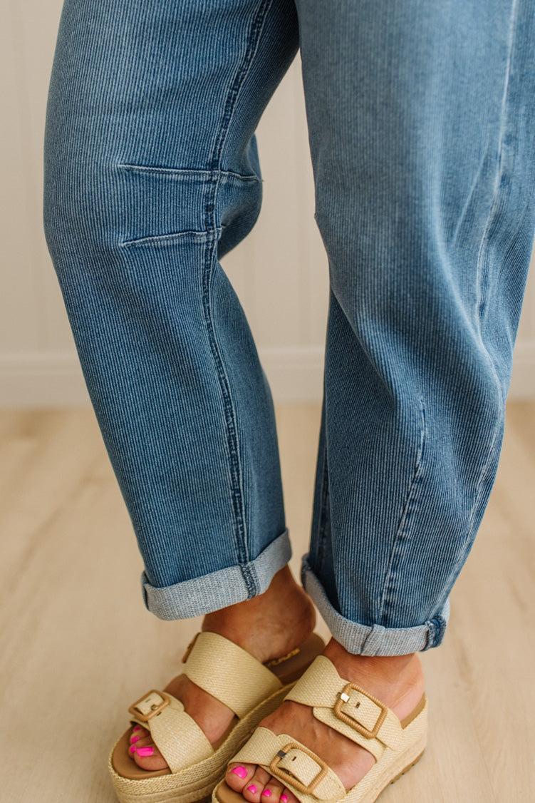 Close-up of blue jeans rolled up at the cuffs with beige sandals on a neutral background