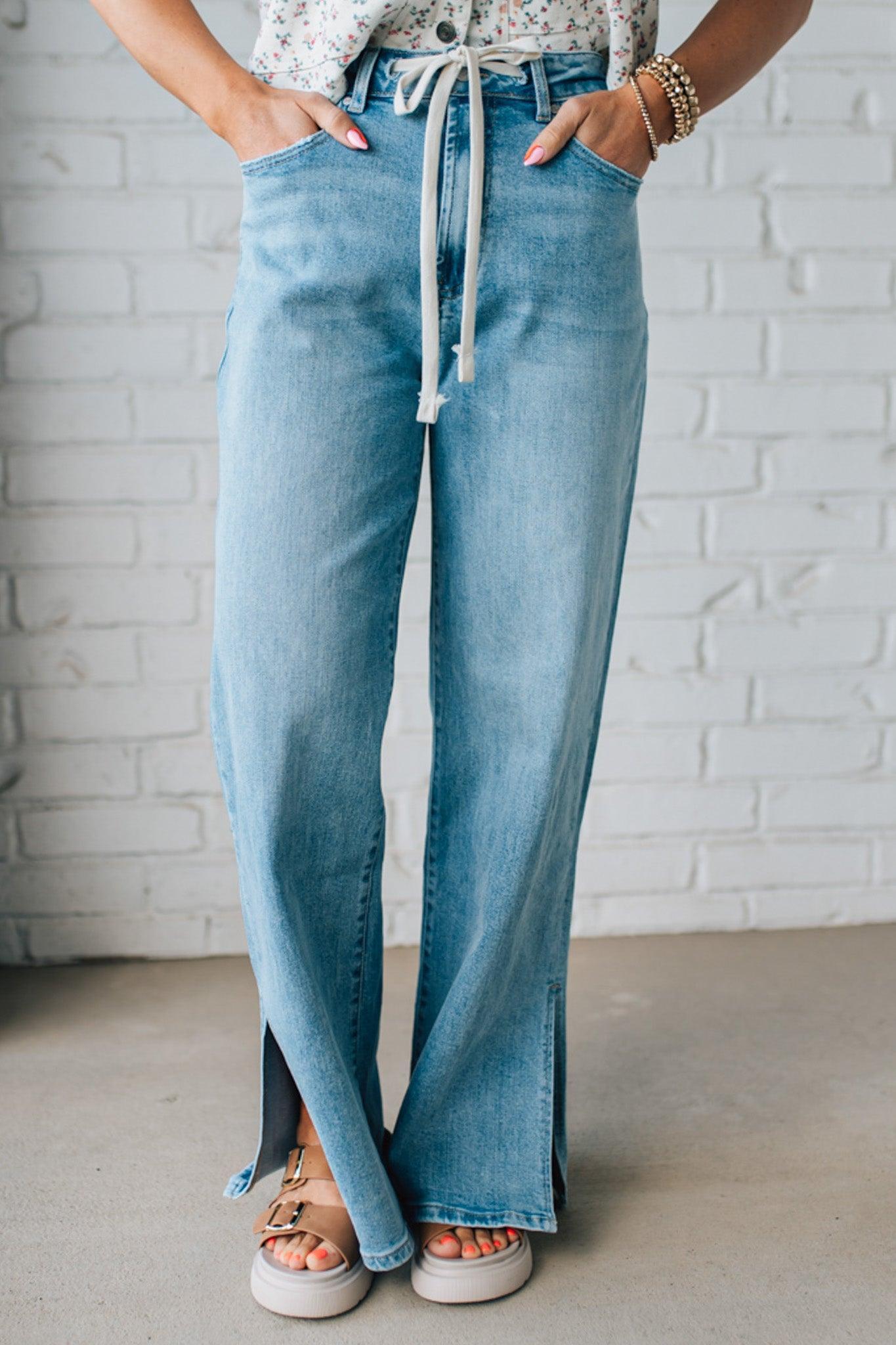 BLONDE WOMAN WEARING DRAWSTRING WAIST DETAIL STRETCH SIDE SLIT WIDE LEG JEAN IN MEDIUM BLUE.