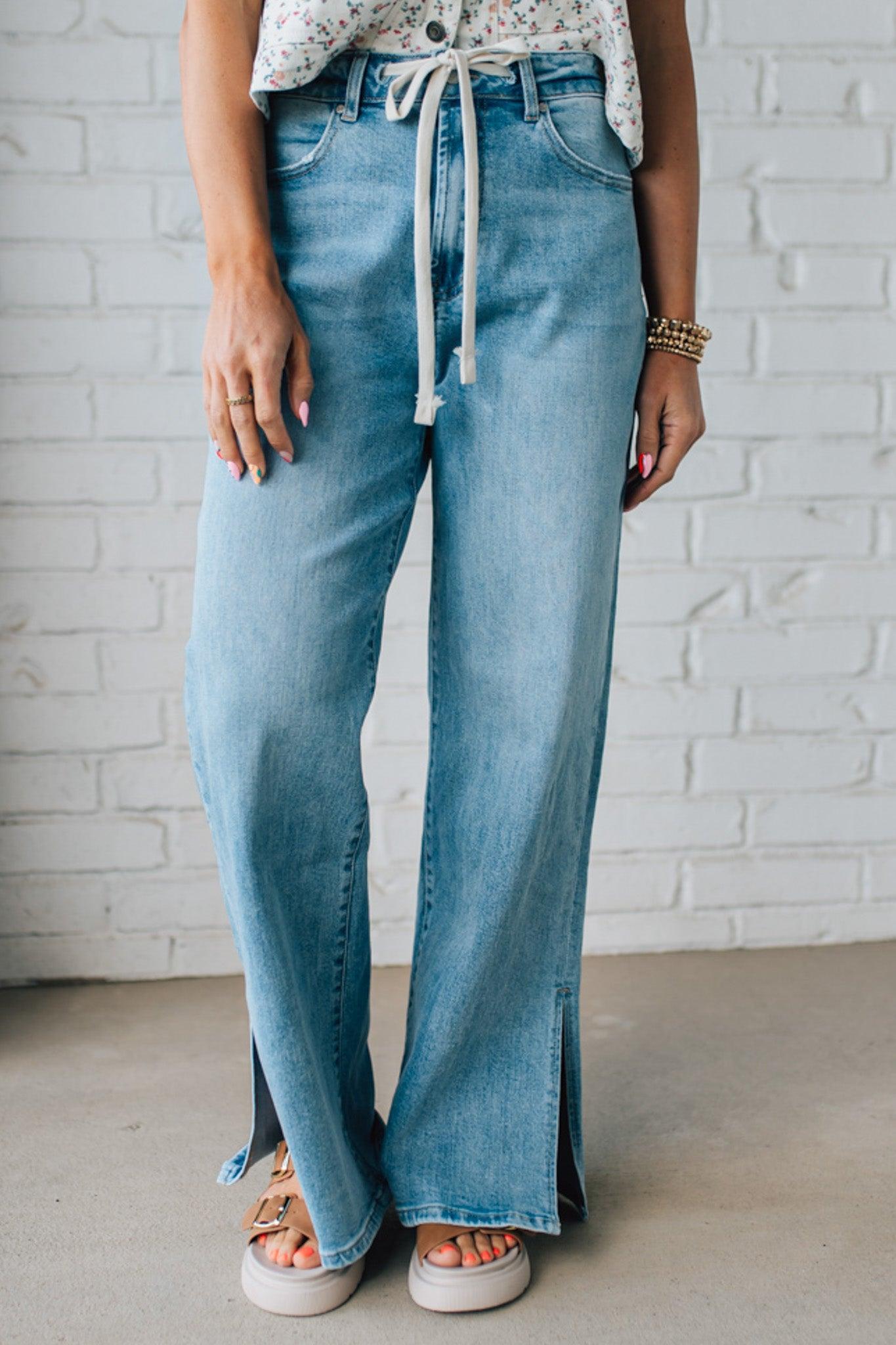 BLONDE WOMAN WEARING DRAWSTRING WAIST DETAIL STRETCH SIDE SLIT WIDE LEG JEAN IN MEDIUM BLUE.