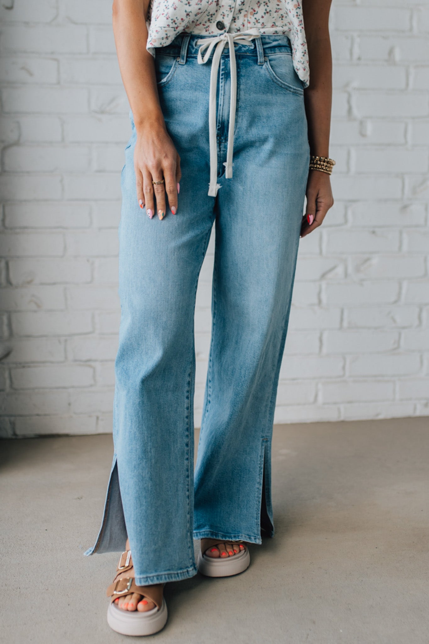 BLONDE WOMAN WEARING DRAWSTRING WAIST DETAIL STRETCH SIDE SLIT WIDE LEG JEAN IN MEDIUM BLUE.