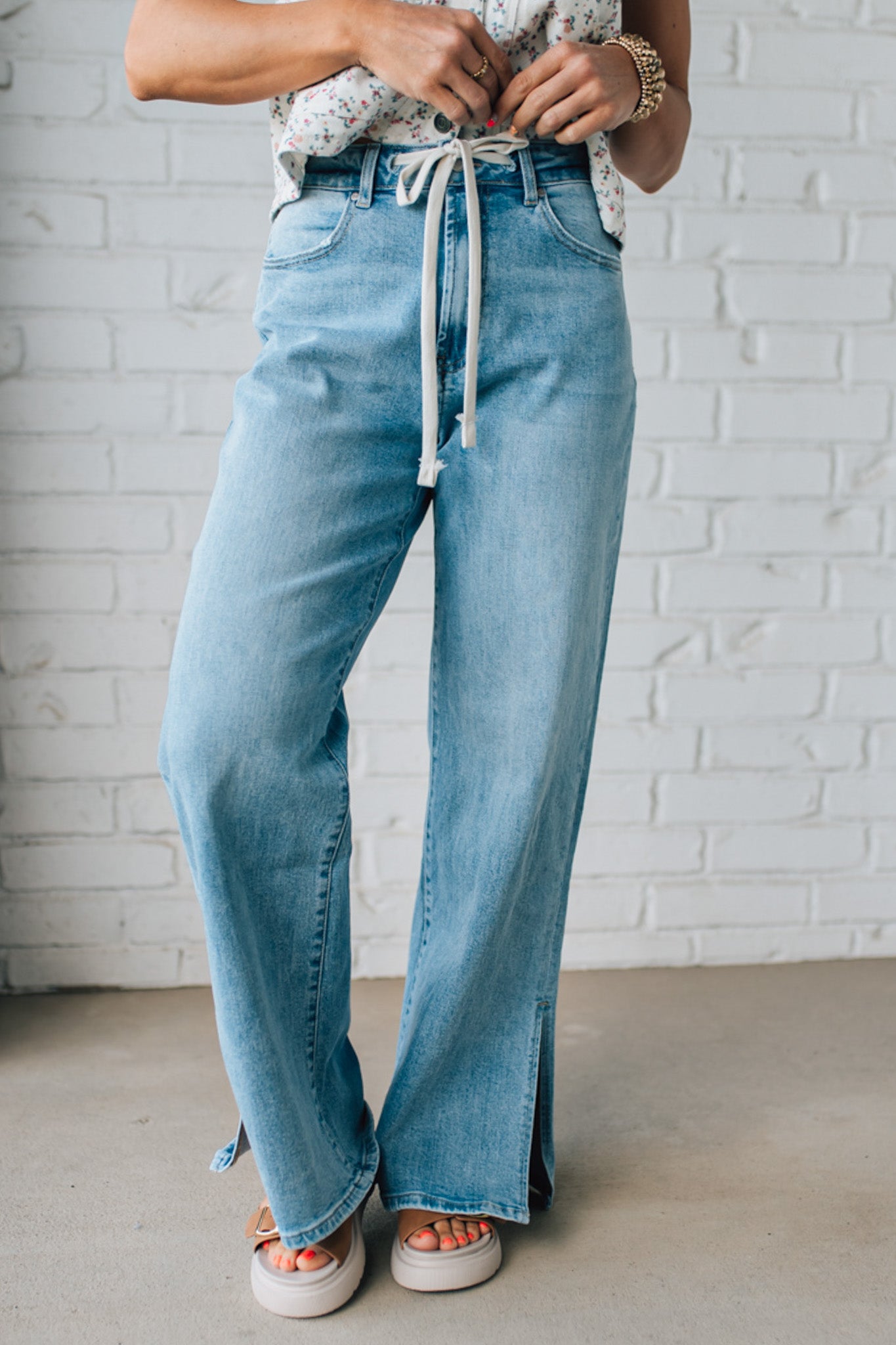 BLONDE WOMAN WEARING DRAWSTRING WAIST DETAIL STRETCH SIDE SLIT WIDE LEG JEAN IN MEDIUM BLUE.