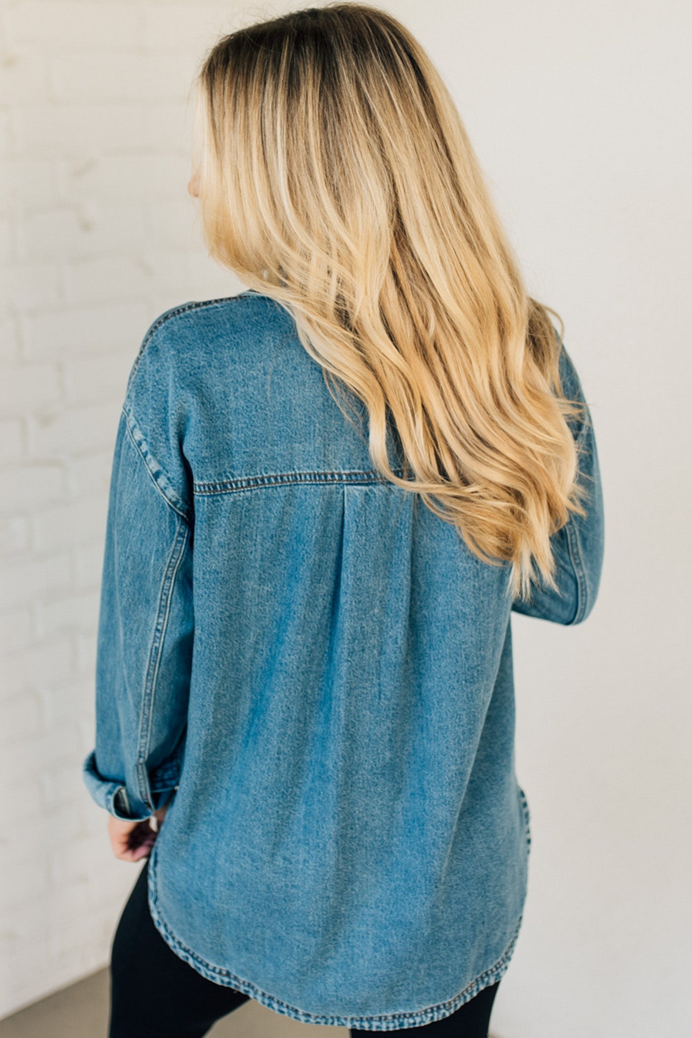 A woman wearing a light blue denim shacket with long sleeves, featuring a round hem and side pockets, buttoned at the front.