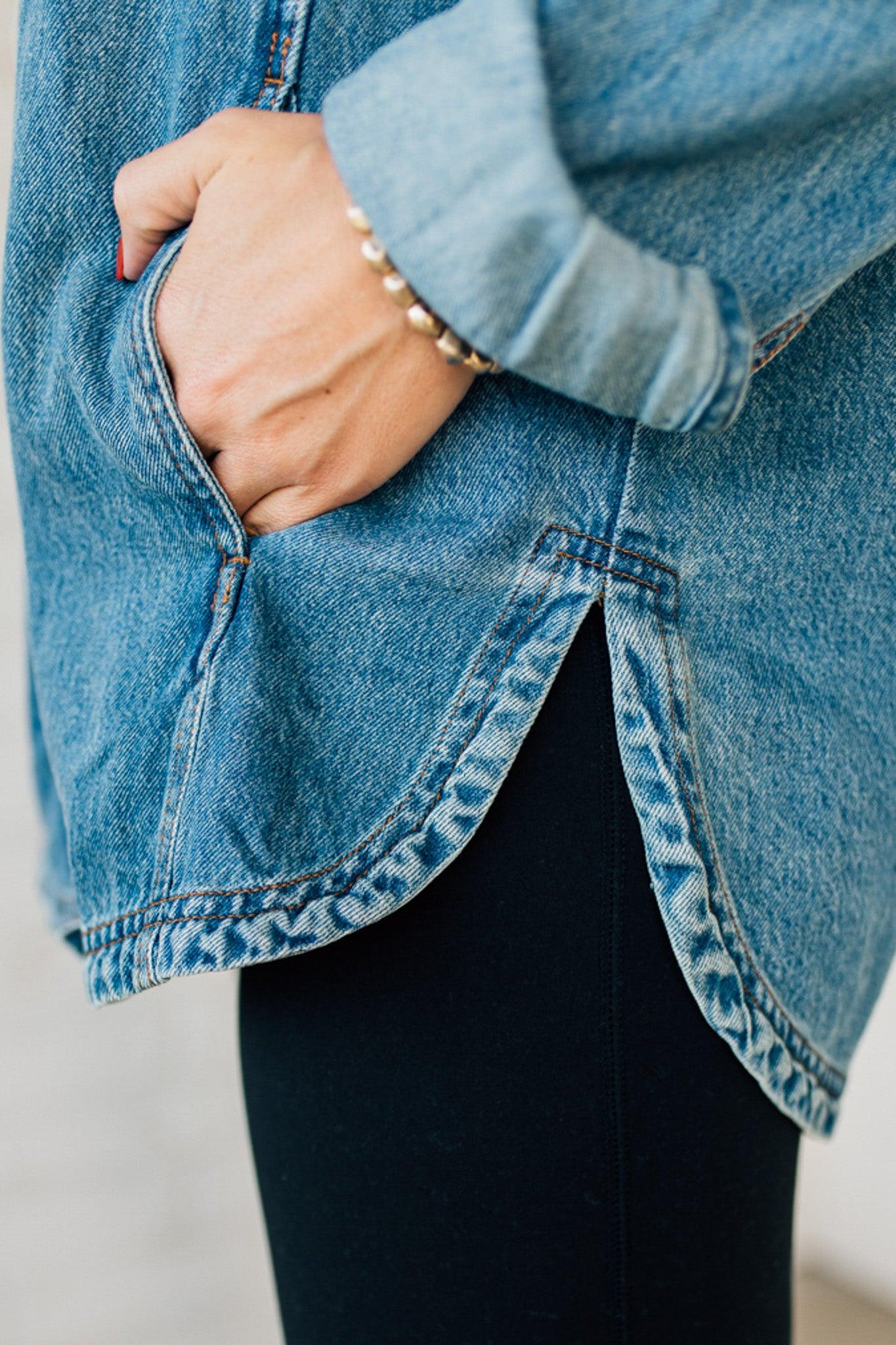 A woman wearing a light blue denim shacket with long sleeves, featuring a round hem and side pockets, buttoned at the front.