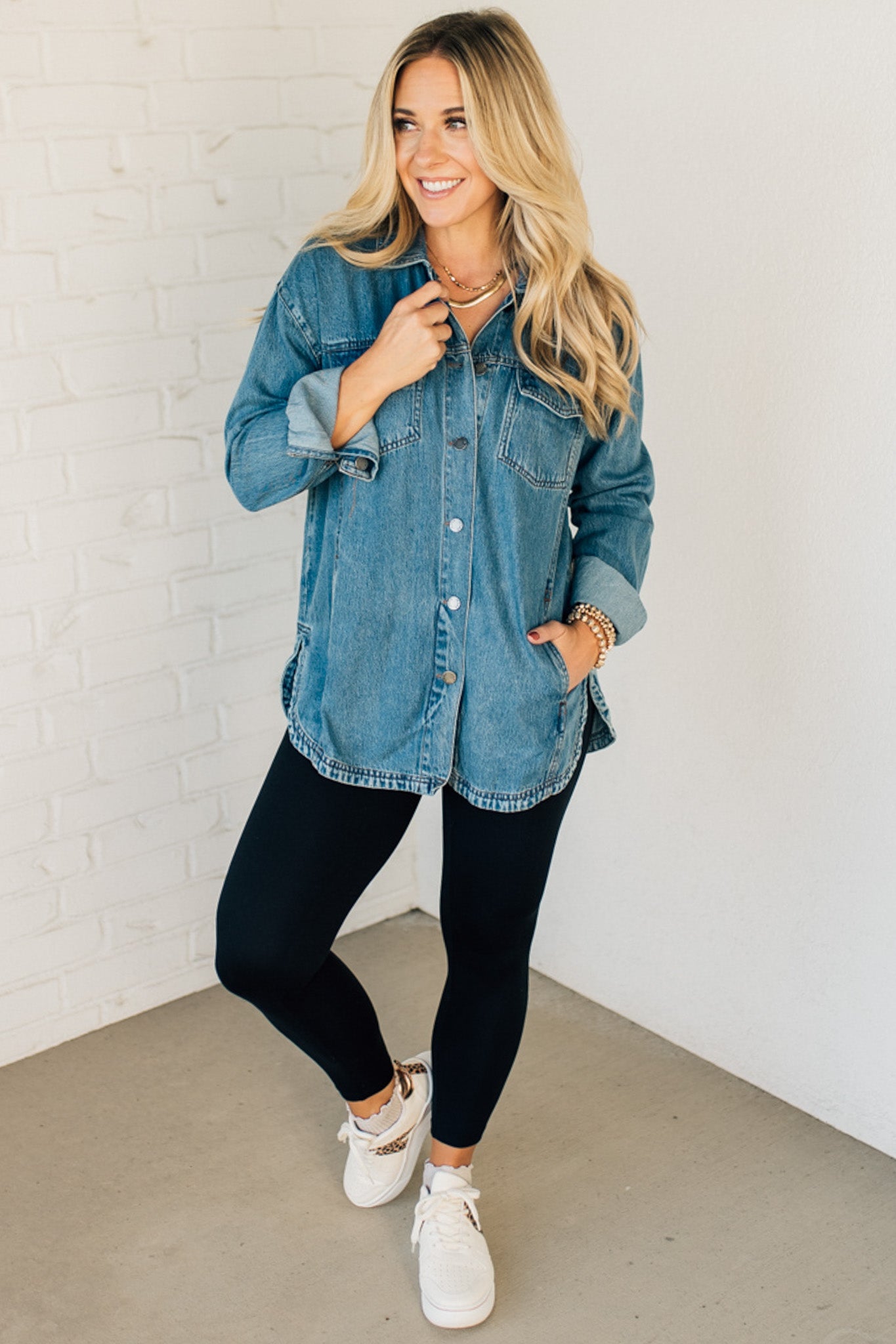 A woman wearing a light blue denim shacket with long sleeves, featuring a round hem and side pockets, buttoned at the front.