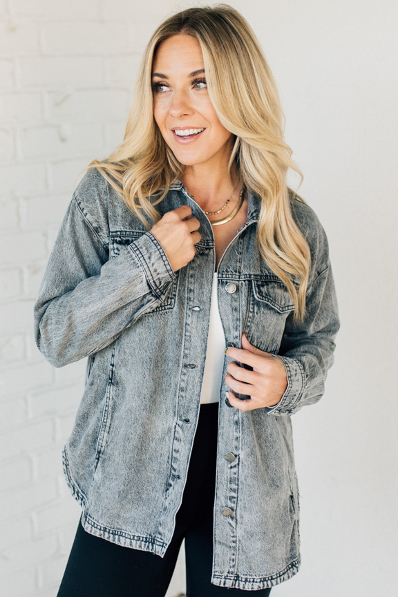 A woman wearing a grey denim shacket with long sleeves, featuring a round hem and side pockets, buttoned at the front.
