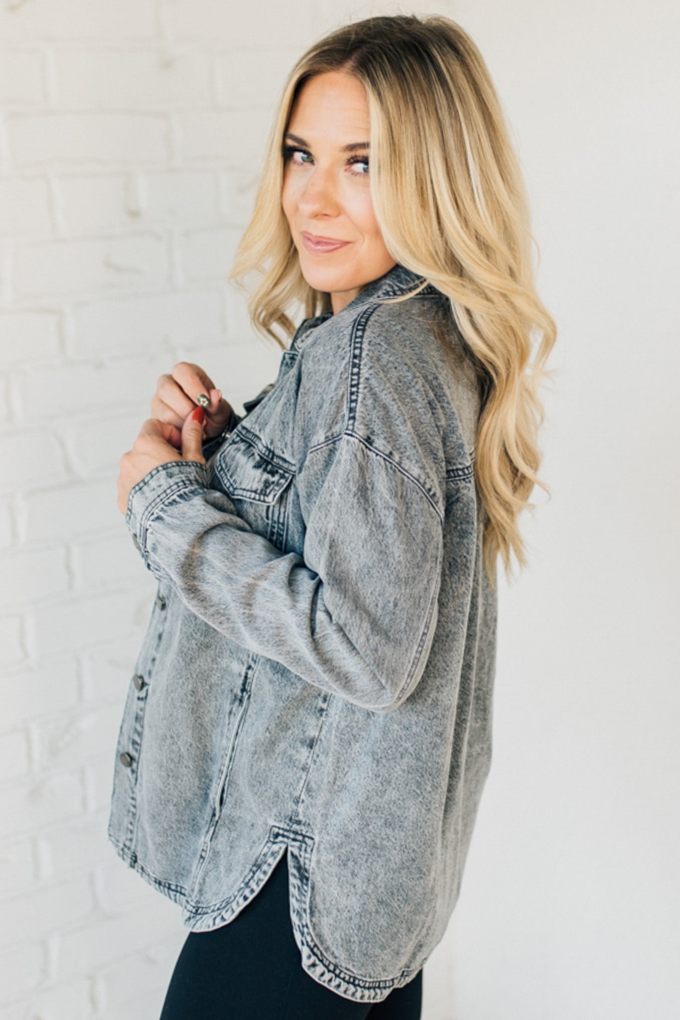 A woman wearing a grey denim shacket with long sleeves, featuring a round hem and side pockets, buttoned at the front.