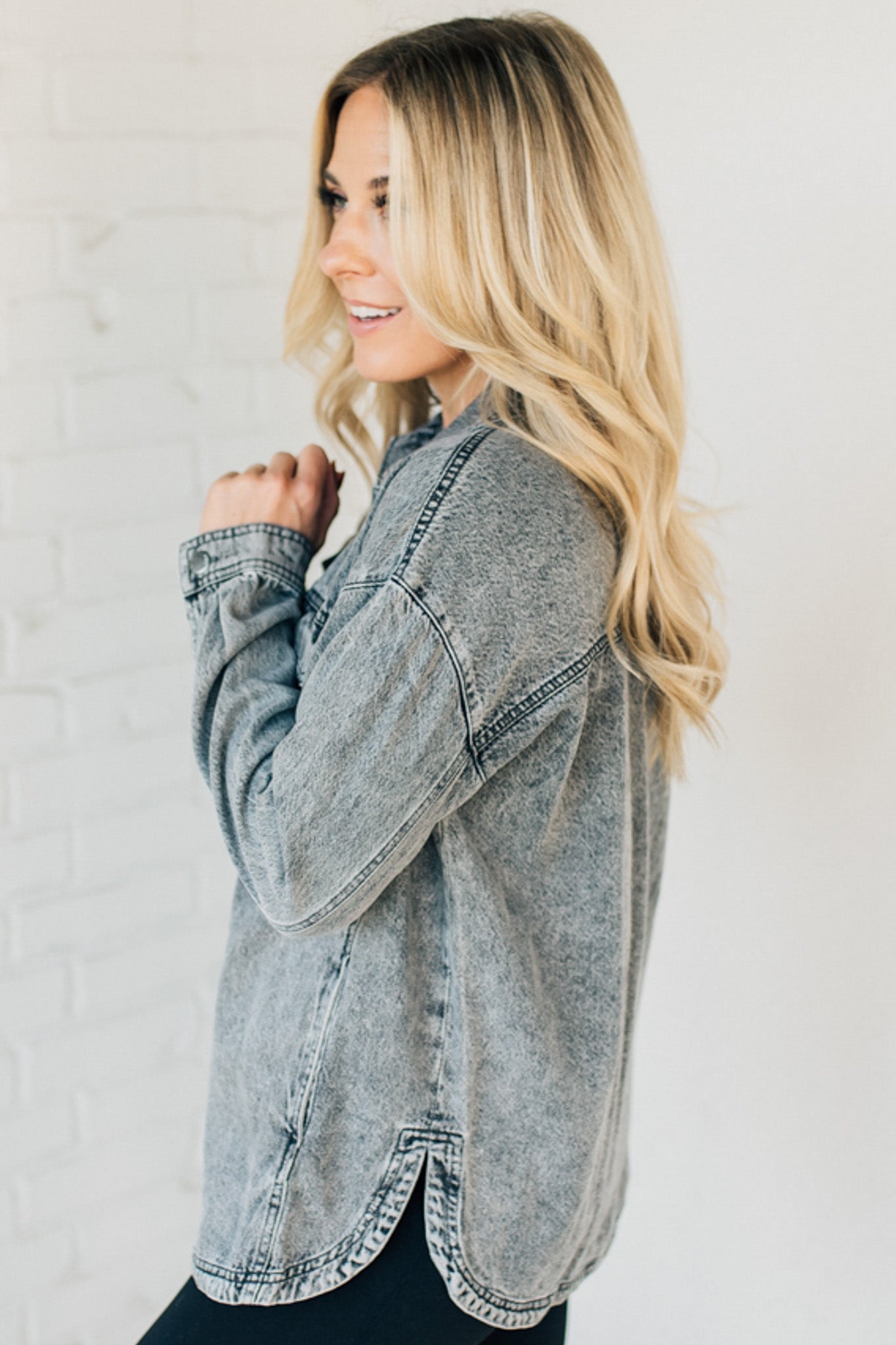 A woman wearing a light grey denim shacket with long sleeves, featuring a round hem and side pockets, buttoned at the front.