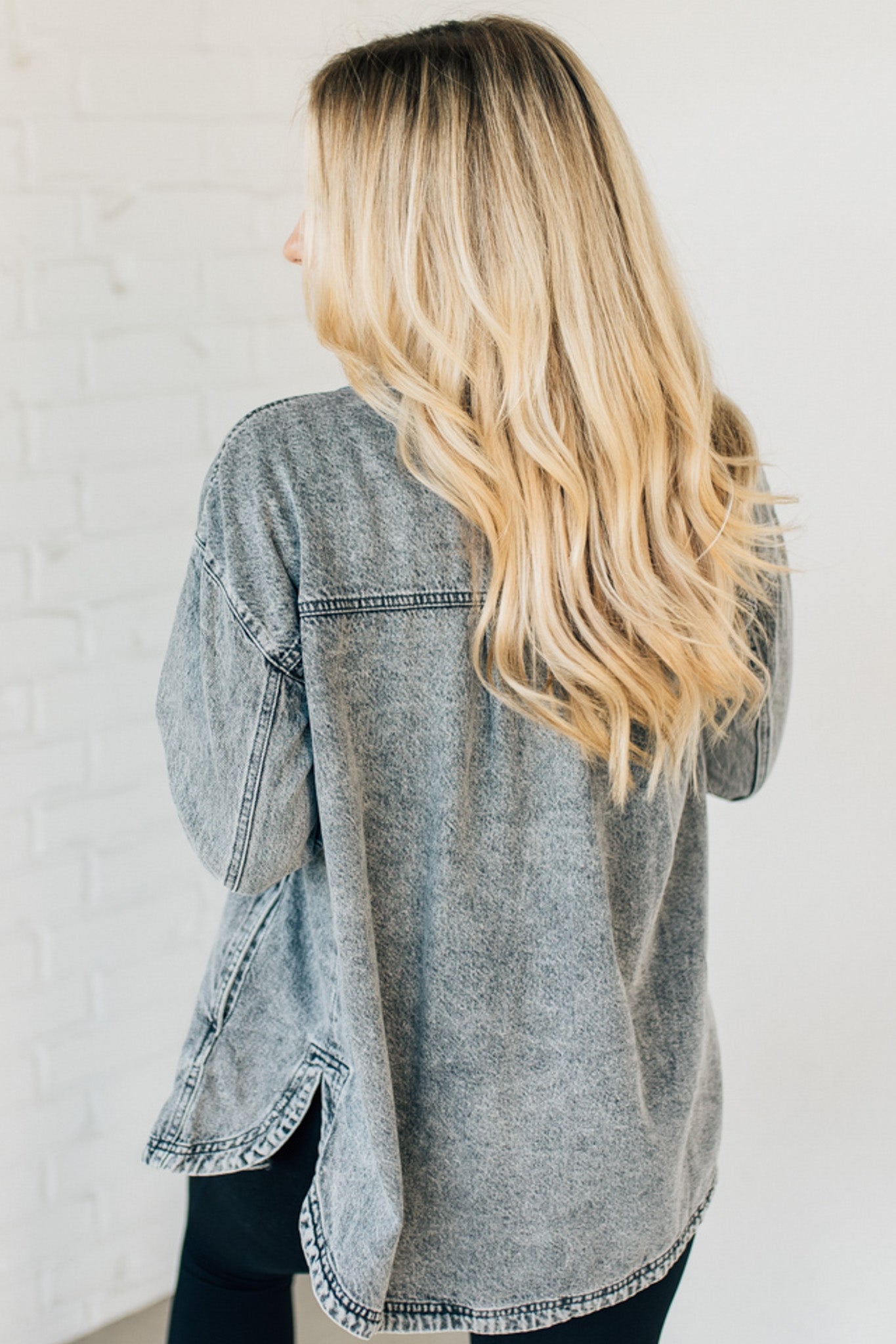 A woman wearing a grey denim shacket with long sleeves, featuring a round hem and side pockets, buttoned at the front.