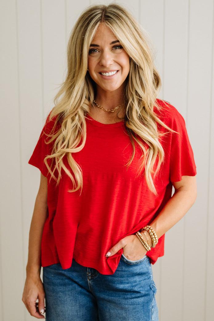 Woman wearing a red shirt and blue jeans against a light wooden panel background