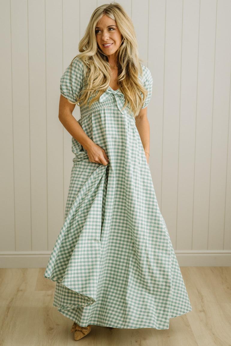 Woman wearing a green checkered dress standing against a beige wall.