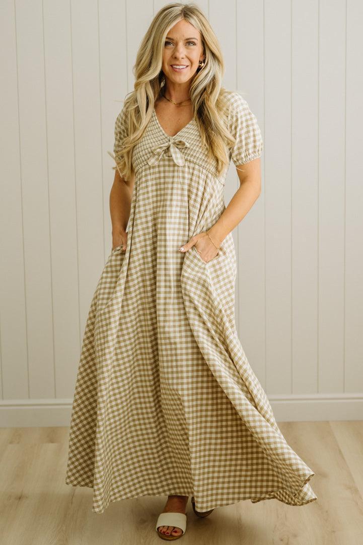 Woman wearing a checkered dress standing against a light wooden paneled wall.
