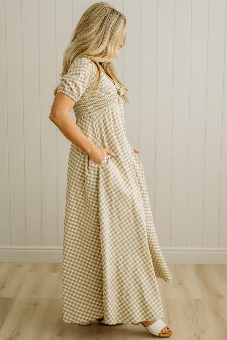 Woman wearing a checkered dress standing against a light wooden paneled wall.