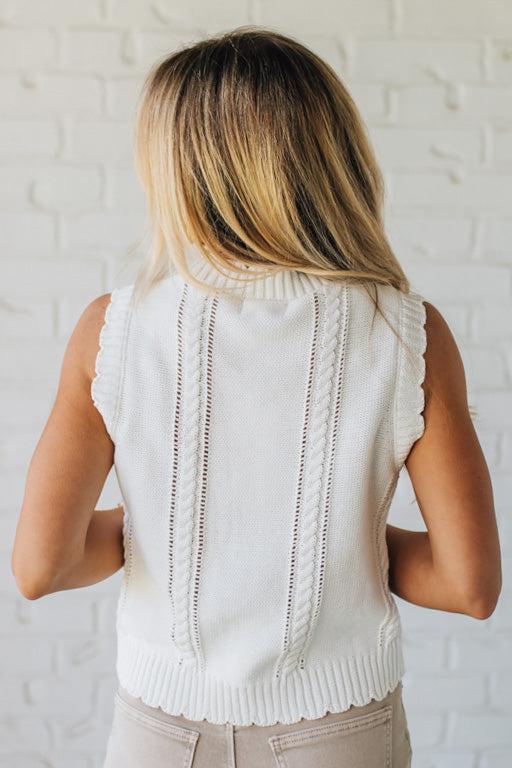 Blonde woman wearing a cream vest with scallop trim and floral embroidery.