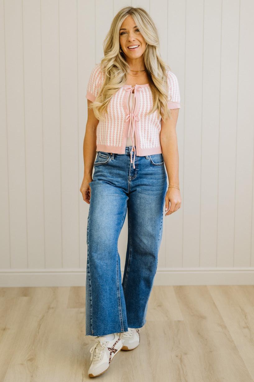 Woman wearing a pink striped top and blue jeans standing against a white paneled wall.