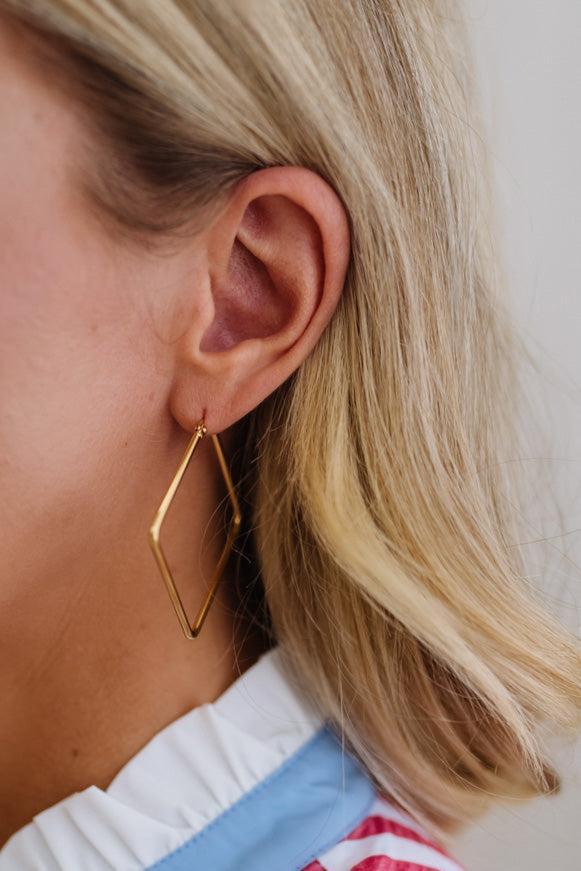 Close-up of a person wearing a gold geometric hoop earring.