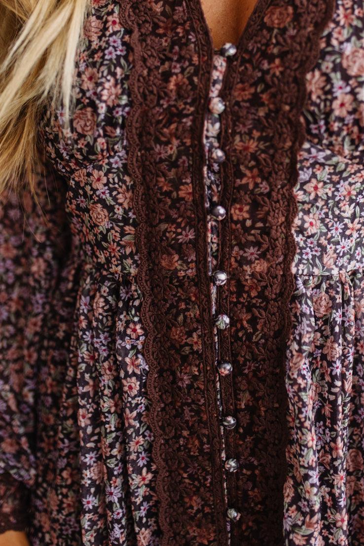 Close-up of a floral long-sleeve top with a dark brown lace front panel and silver buttons, worn by a model.