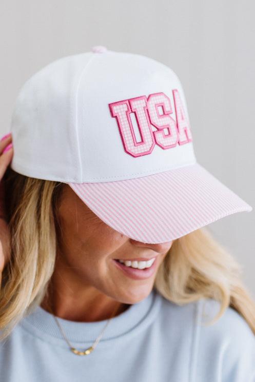 White cap with pink brim and 'USA' text worn by a person on a light gray background