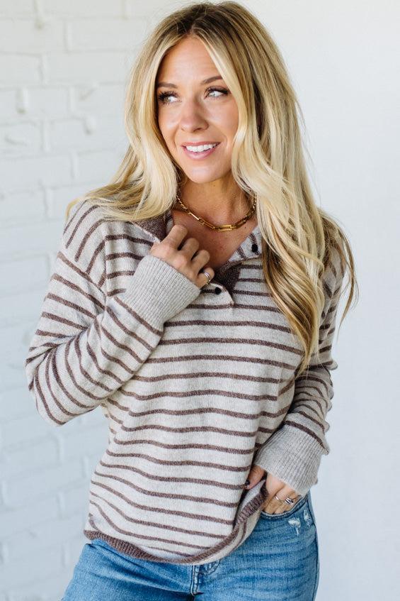 Woman wearing a striped sweater and jeans against a white brick wall.
