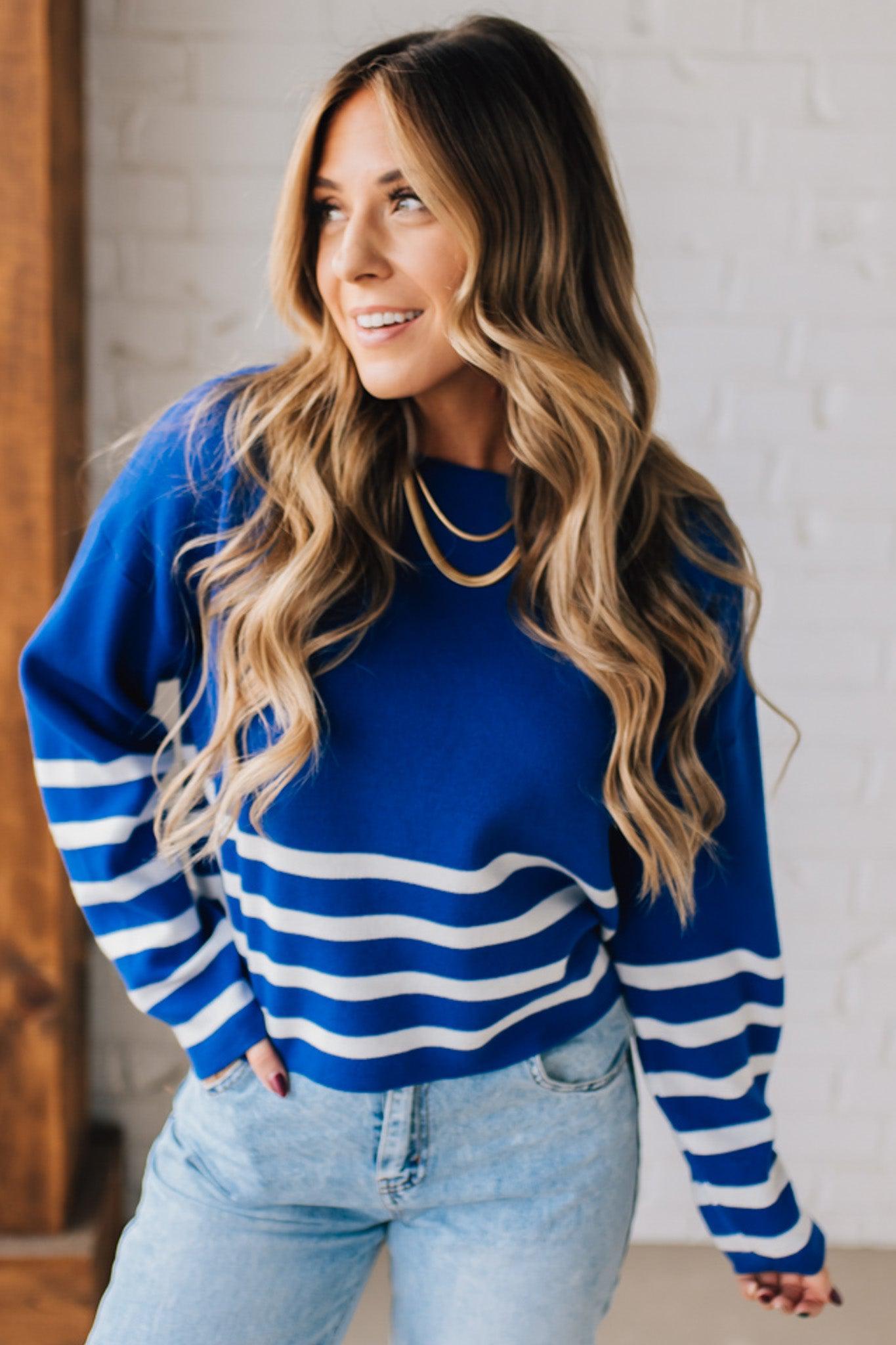 Blonde woman modeling a royal blue waist length sweater with white stripes on the bottom half