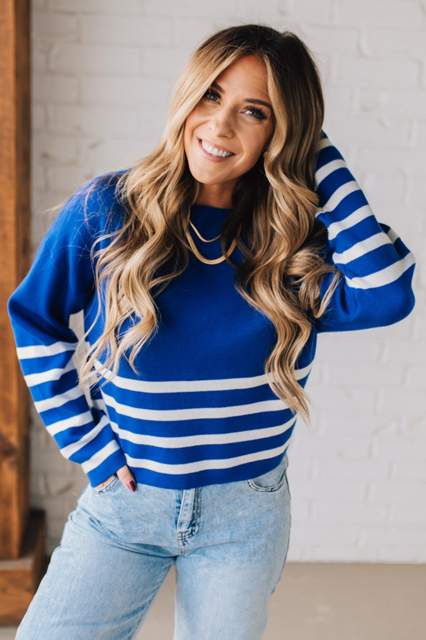 Blonde woman modeling a royal blue waist length sweater with white stripes on the bottom half