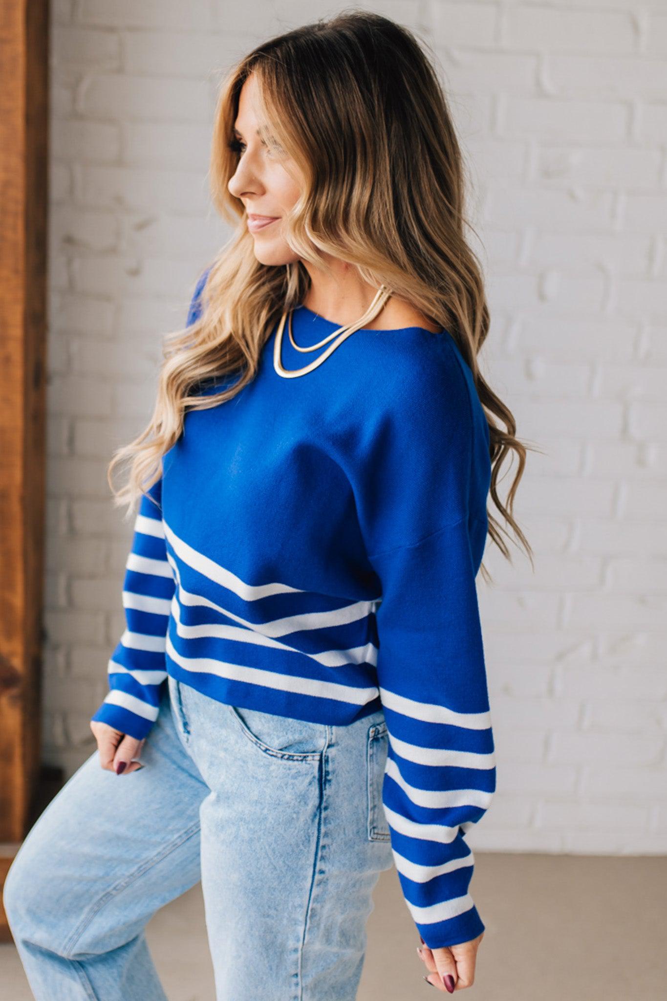 Blonde woman modeling a royal blue waist length sweater with white stripes on the bottom half