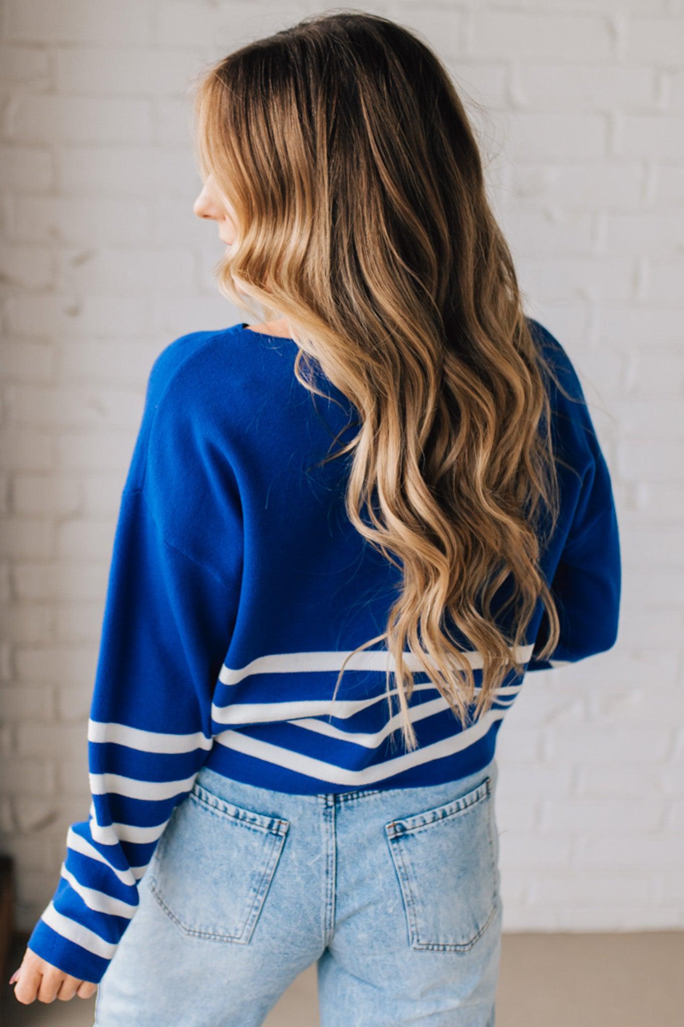 Blonde woman modeling a royal blue waist length sweater with white stripes on the bottom half