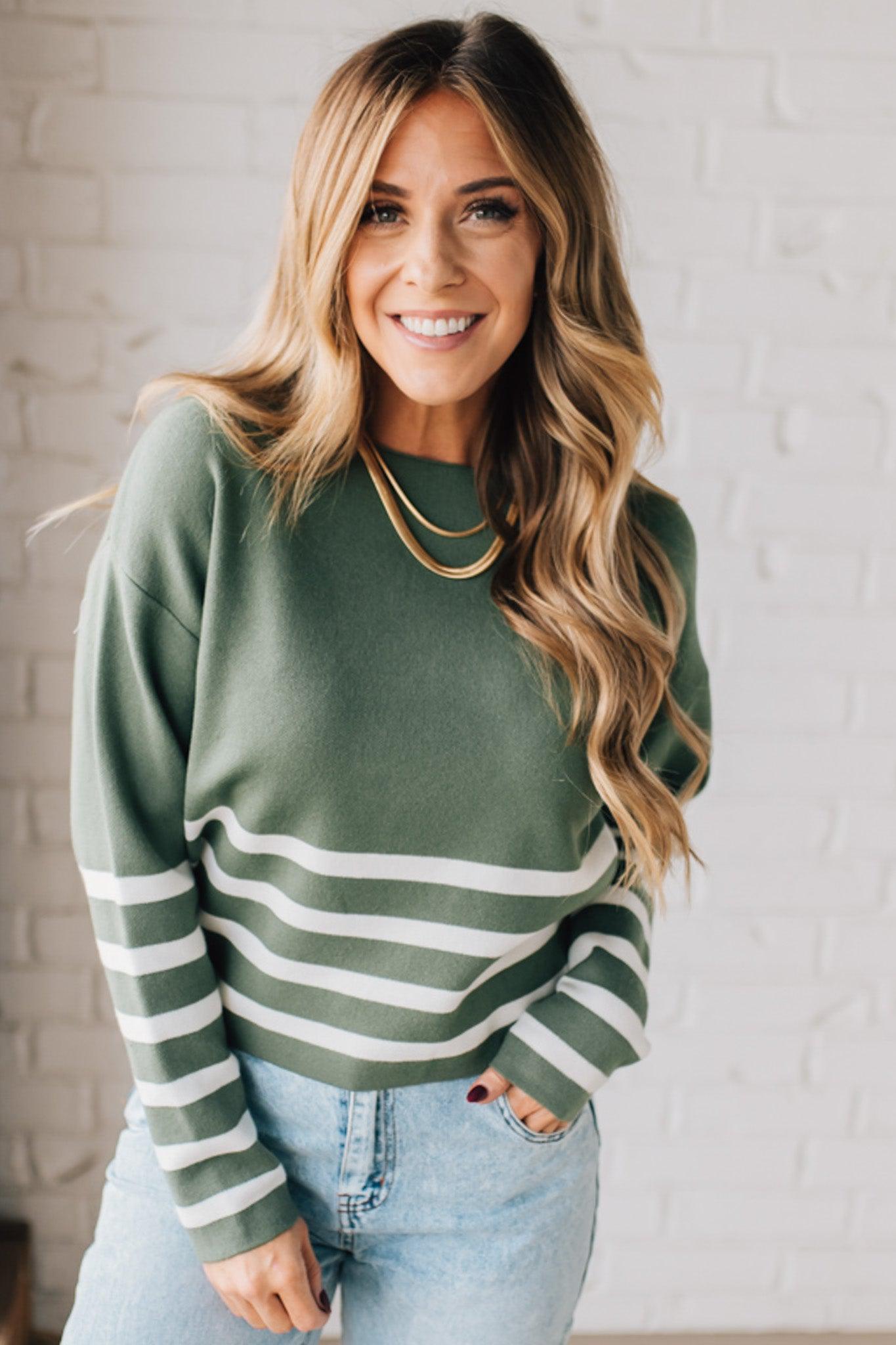 Blonde woman modeling an olive green waist length sweater with ivory stripes on the bottom half