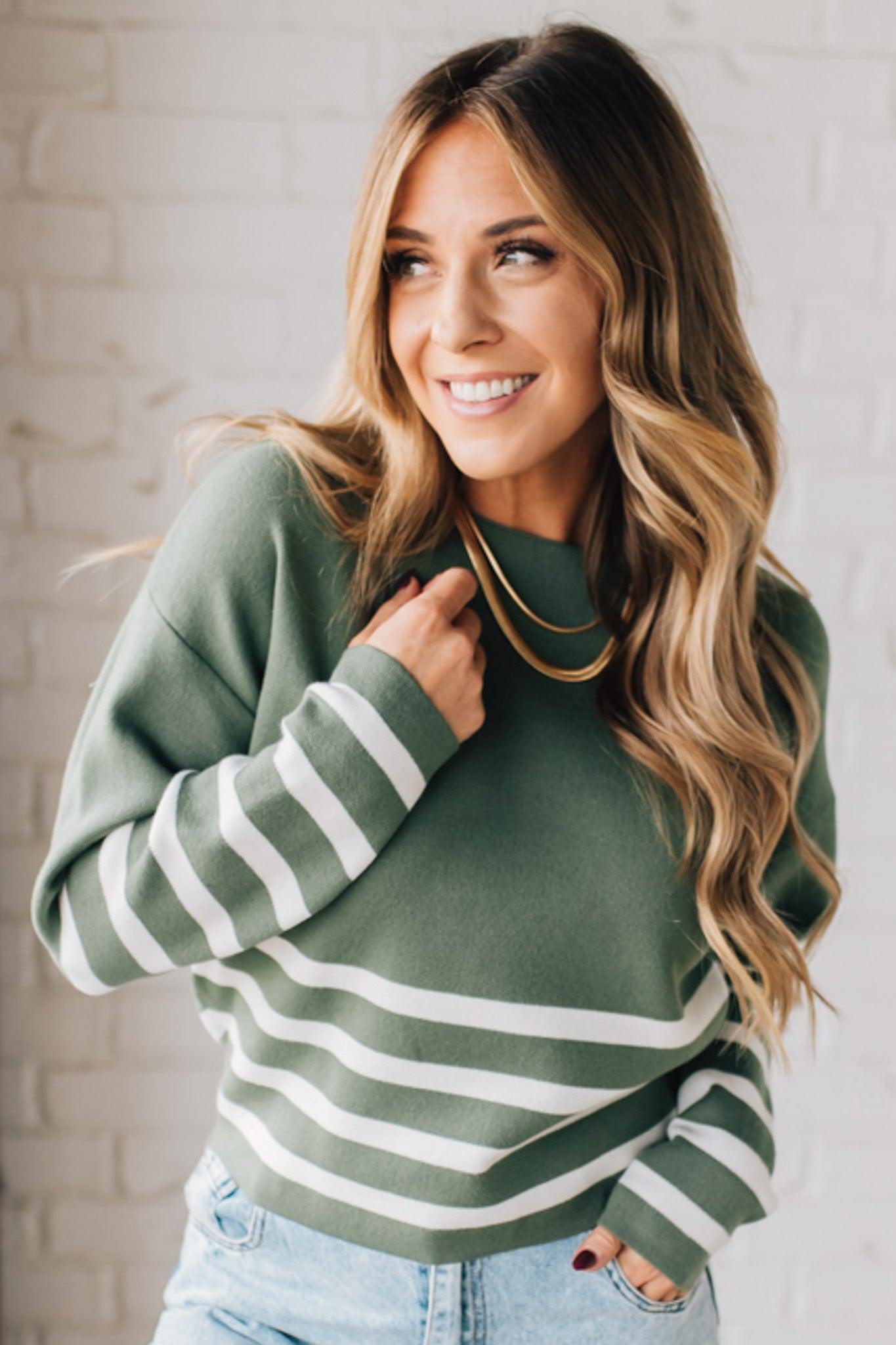 Blonde woman modeling an olive green waist length sweater with ivory stripes on the bottom half