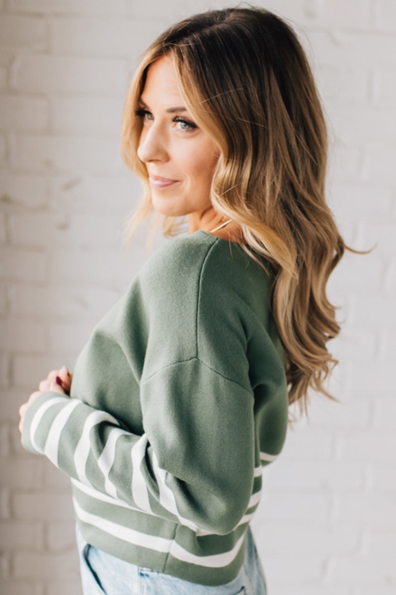 Blonde woman modeling an olive green waist length sweater with ivory stripes on the bottom half