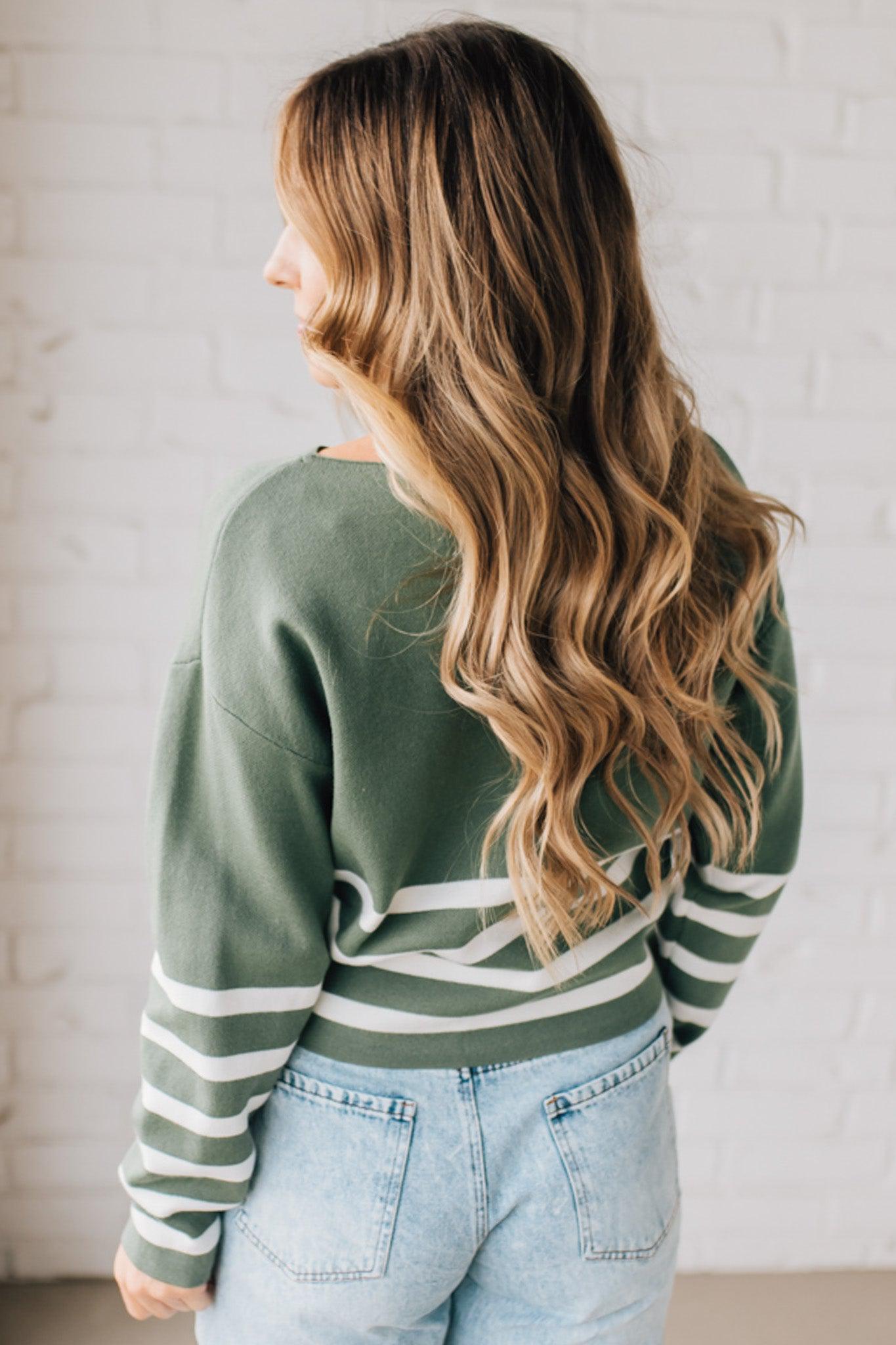 Blonde woman modeling an olive green waist length sweater with ivory stripes on the bottom half