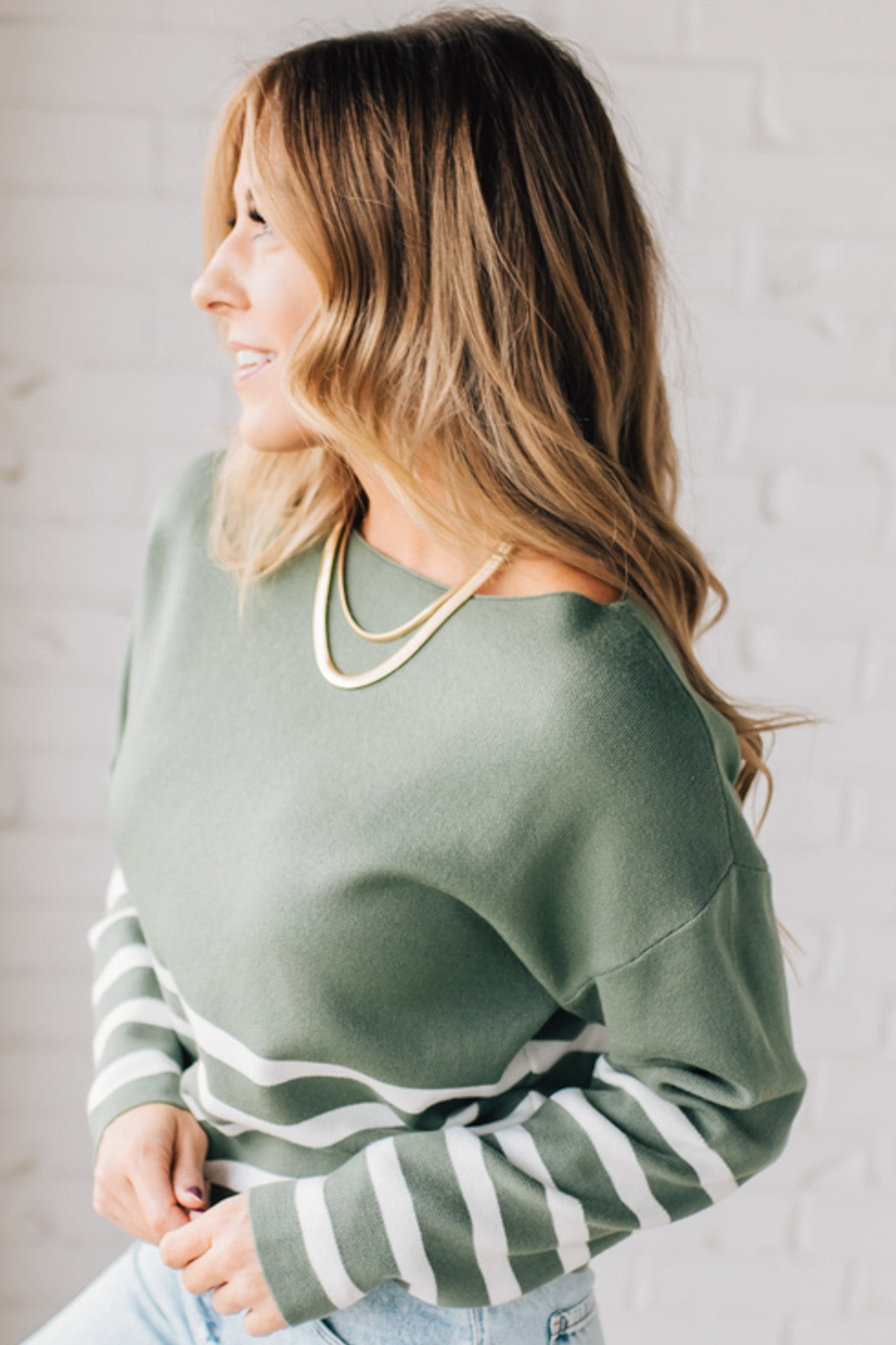 Blonde woman modeling an olive green waist length sweater with ivory stripes on the bottom half