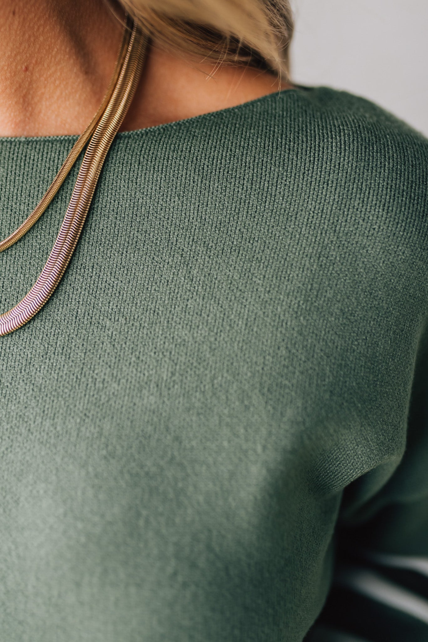 Blonde woman modeling an olive green waist length sweater with ivory stripes on the bottom half