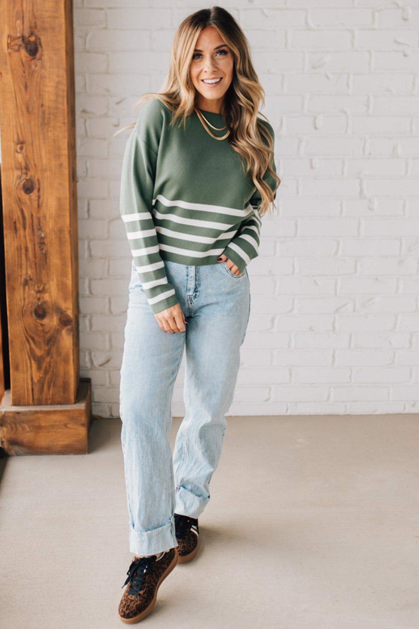 Blonde woman modeling an olive green waist length sweater with ivory stripes on the bottom half