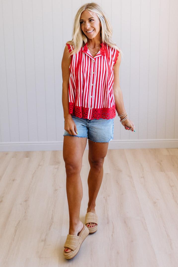 Woman wearing a red and white striped sleeveless shirt with denim shorts on a light wooden floor.