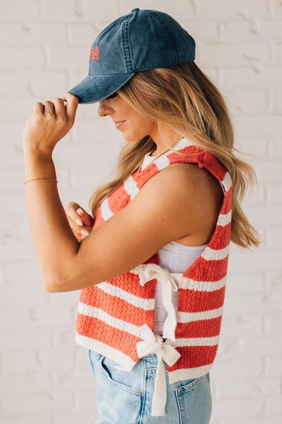 Blonde woman in a hat and shorts wearing a red striped sweater tank with double side ties.