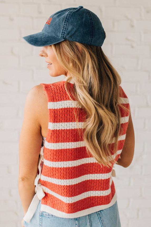 Blonde woman in a hat and shorts wearing a red striped sweater tank with double side ties.