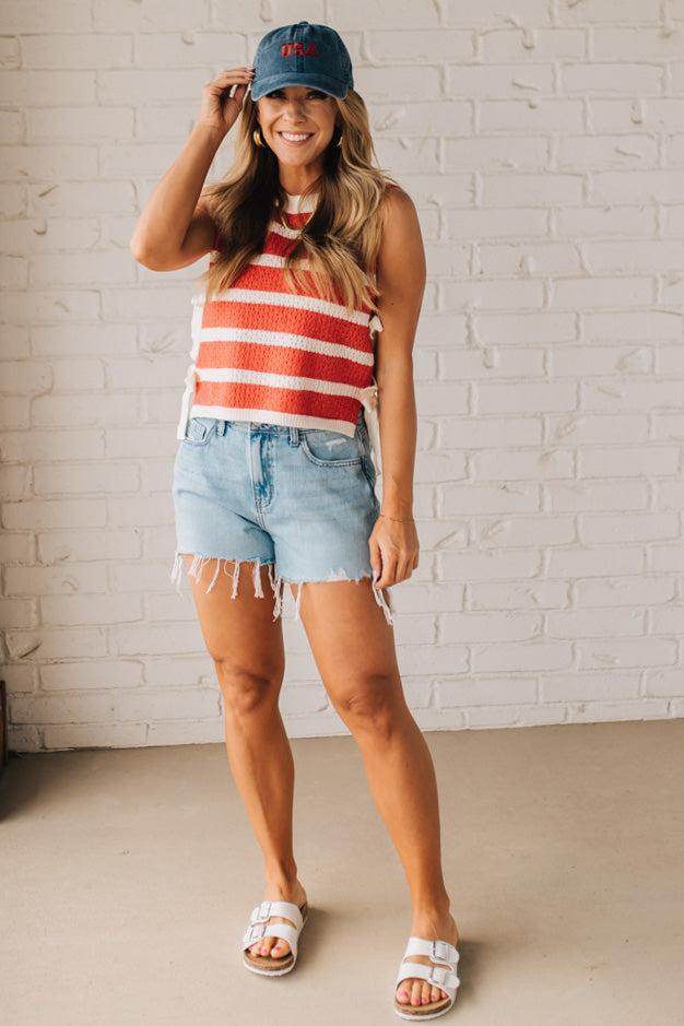 Blonde woman in a hat and shorts wearing a red striped sweater tank with double side ties.