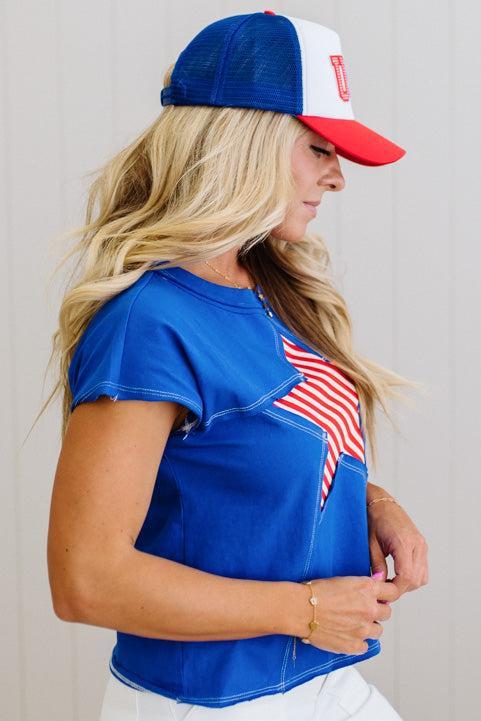Woman wearing a blue t-shirt with an American flag design and a red, white, and blue cap.