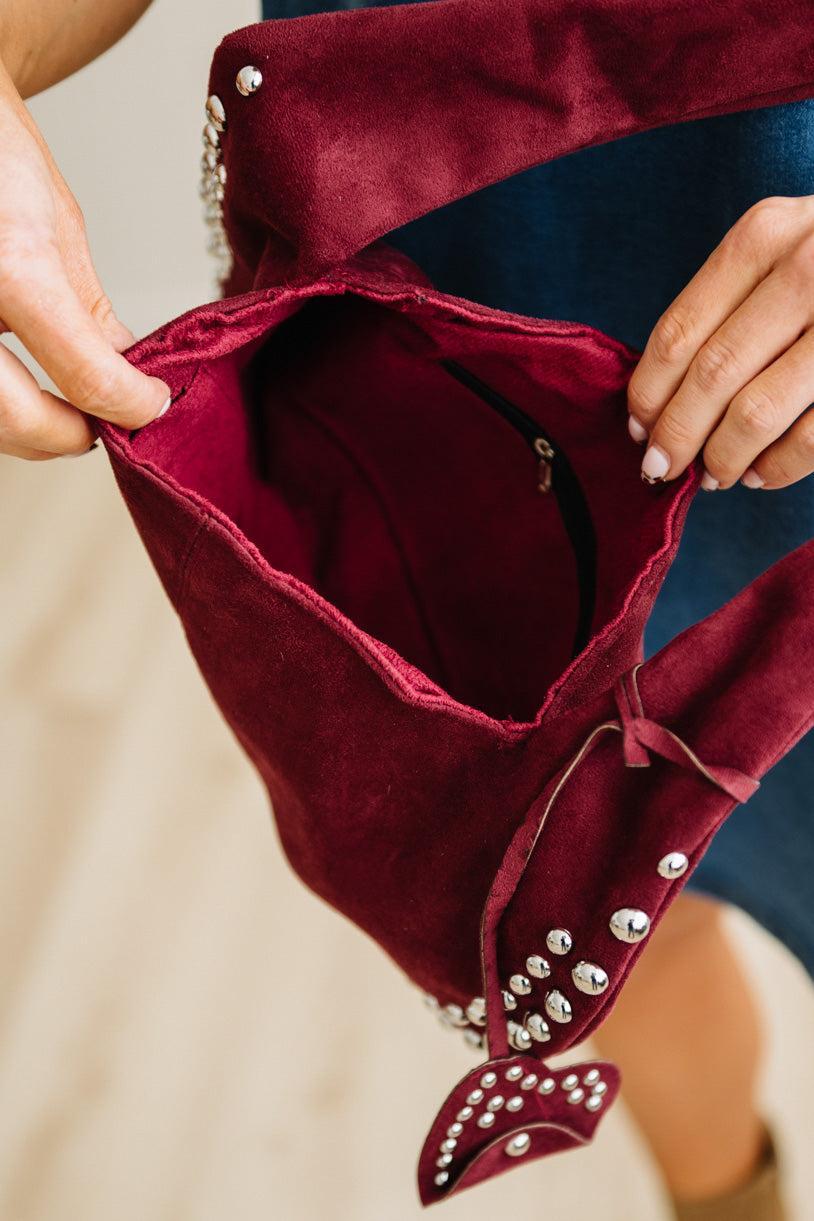 Close-up of a burgundy velvet handbag with silver studs held by a person.