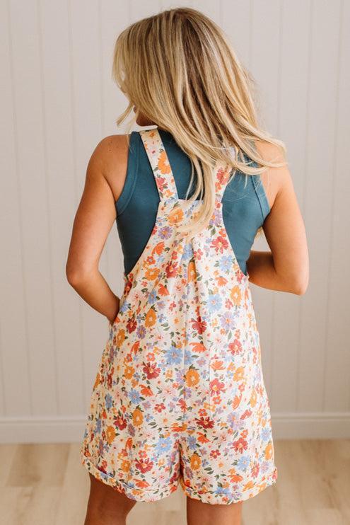 Woman wearing a floral overalls dress against a neutral background