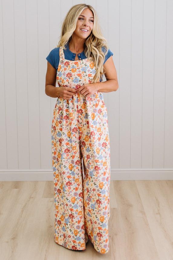 Woman wearing a floral jumpsuit with a blue top against a white paneled wall.