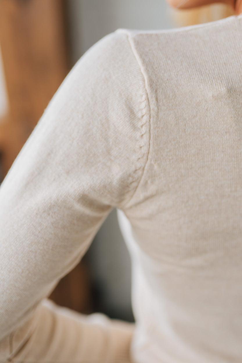 Close-up of a person wearing a beige long-sleeve shirt with a blurred background