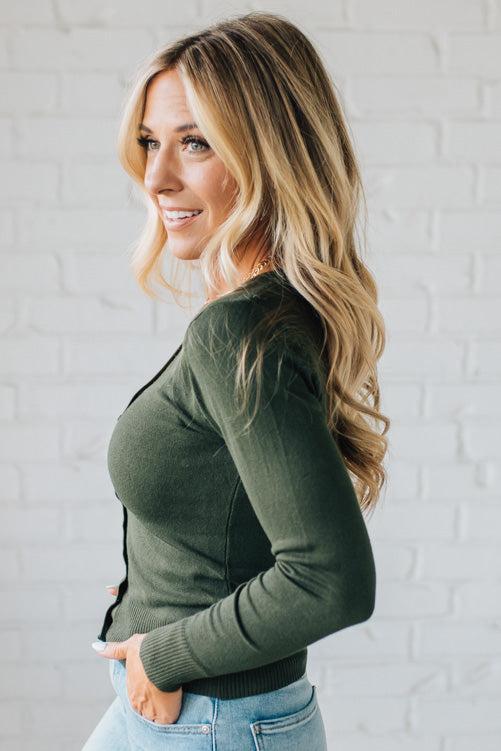 Woman wearing a green cardigan against a white brick wall