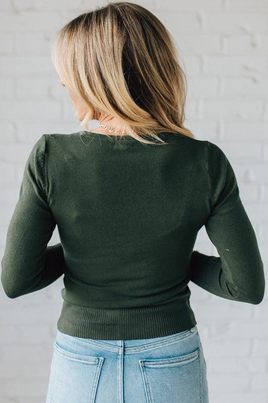 Person wearing a green sweater and blue jeans against a light gray background