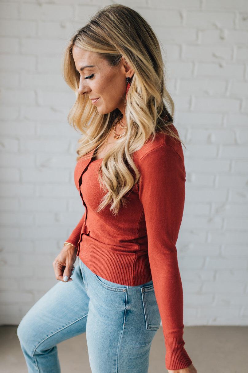 Woman wearing a red sweater and blue jeans against a white brick wall.