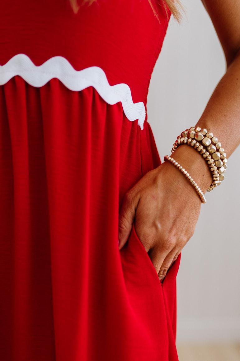 Red dress with white trim worn by a person, focusing on the dress and hand with bracelets.