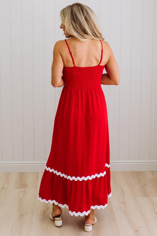 Woman wearing a red dress with white trim against a light wooden floor and white wall background
